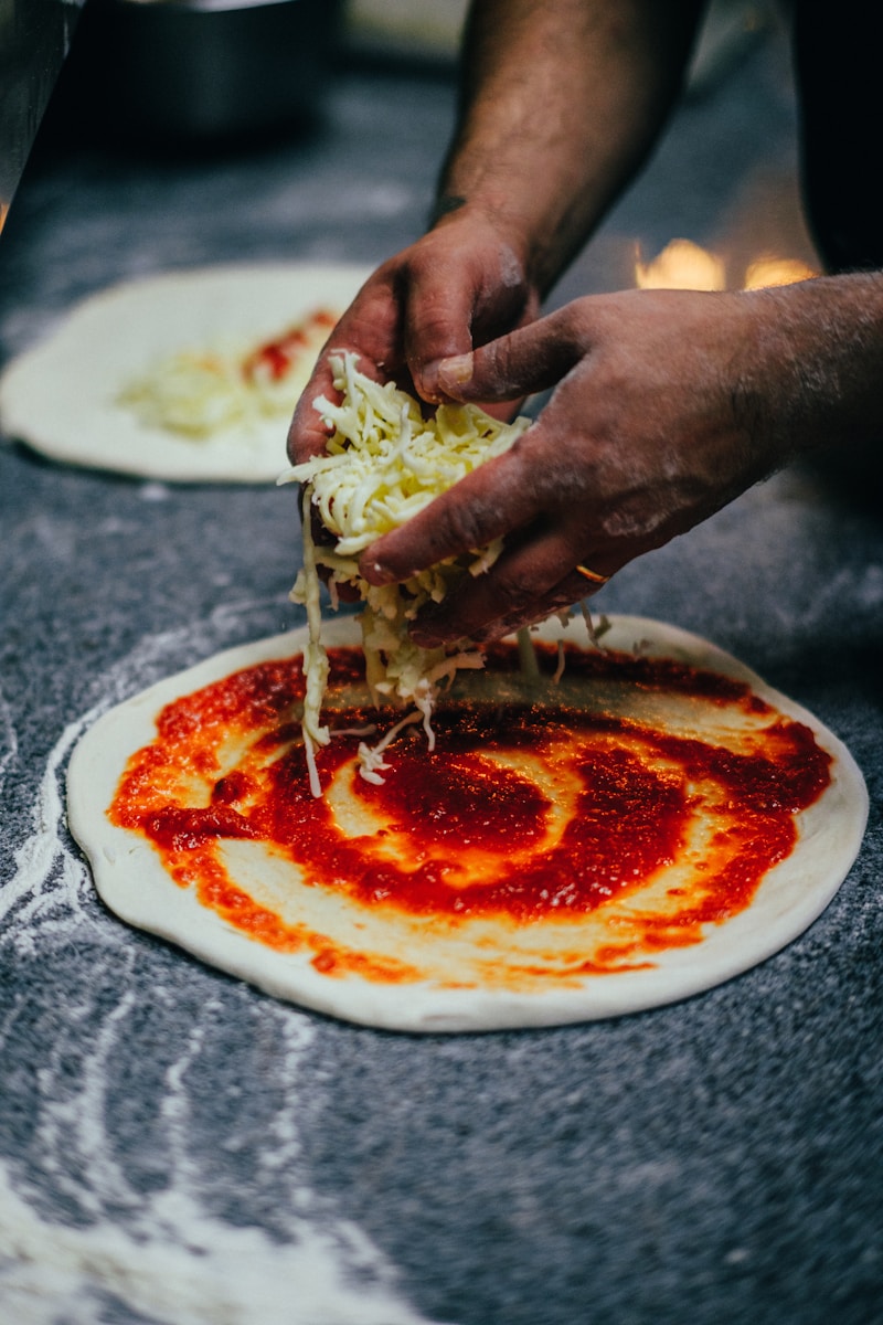 Photo by Mathias Reding a person is putting sauce on a pizza